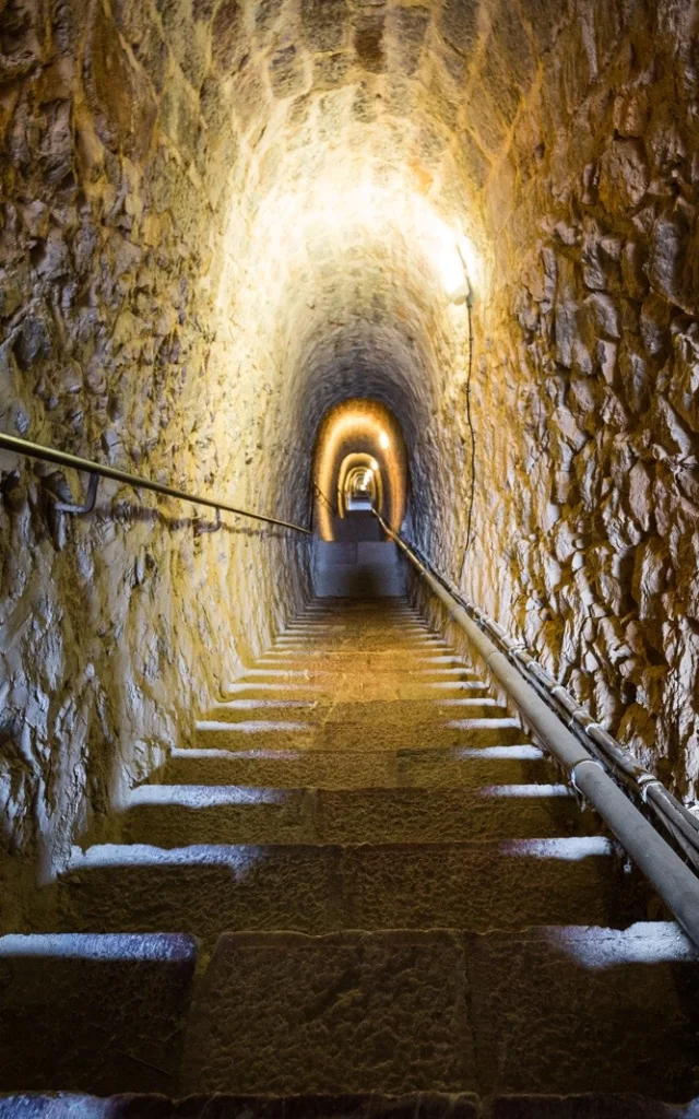 Escalier souterrain des Mille Marches, long passage voûté en pierre éclairé par des lampes murales, reliant le Fort Libéria à Villefranche-de-Conflent.