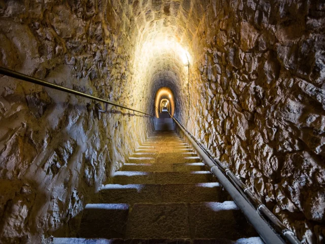 Escalier souterrain des Mille Marches, long passage voûté en pierre éclairé par des lampes murales, reliant le Fort Libéria à Villefranche-de-Conflent.