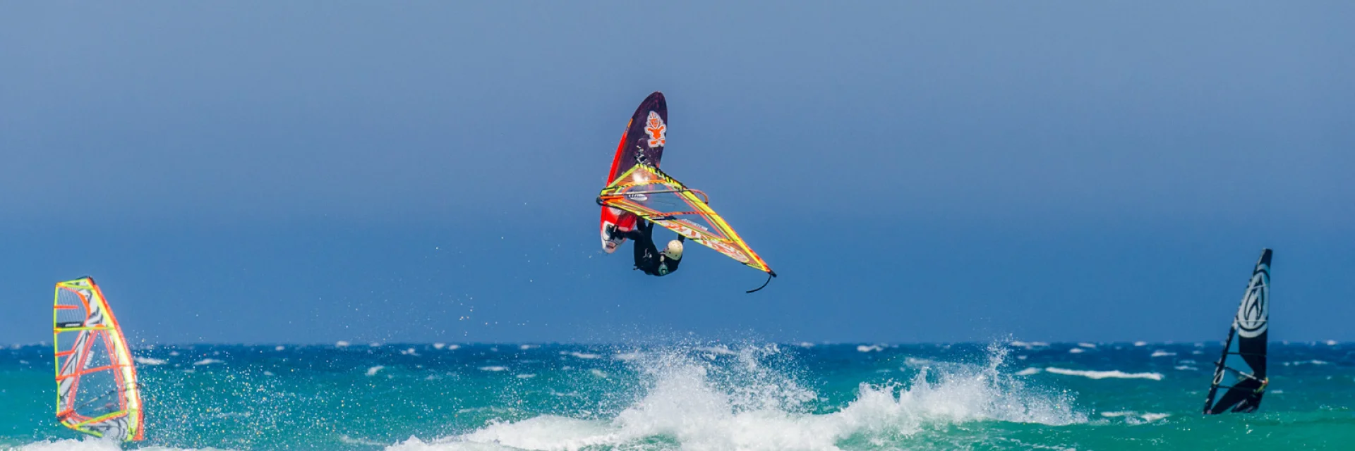 Planche à voile effectuant une figure au-dessus des vagues par temps venté.