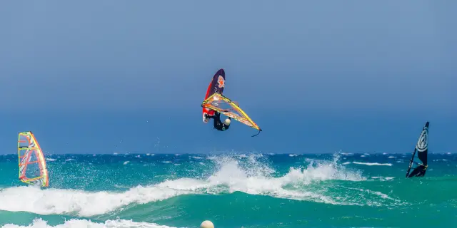 Planche à voile effectuant une figure au-dessus des vagues par temps venté.