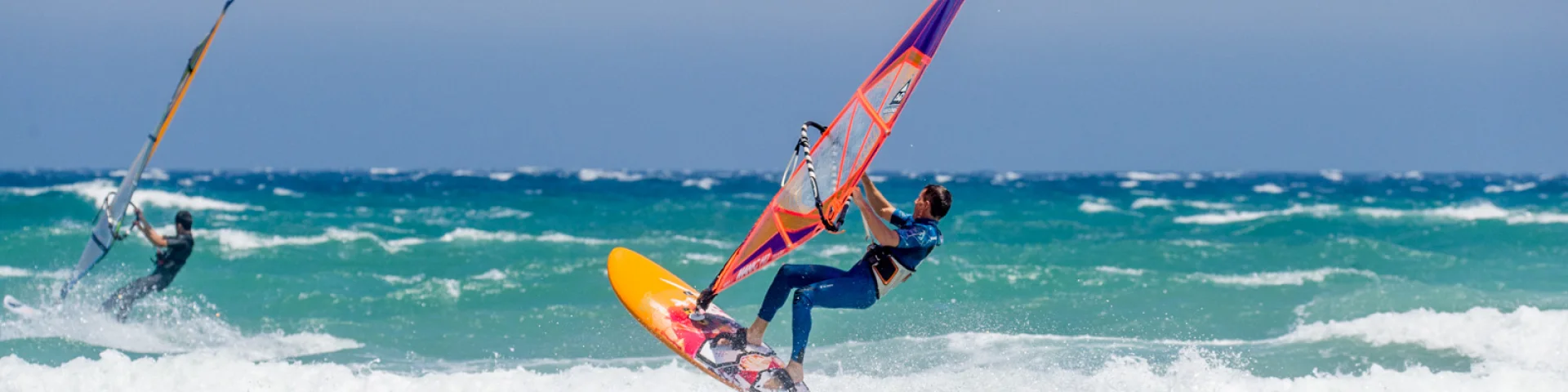 Planche à voile en action sur une mer agitée avec un pratiquant réalisant une figure sur les vagues.