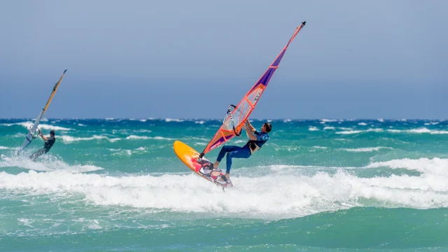 Planche à voile en action sur une mer agitée avec un pratiquant réalisant une figure sur les vagues.