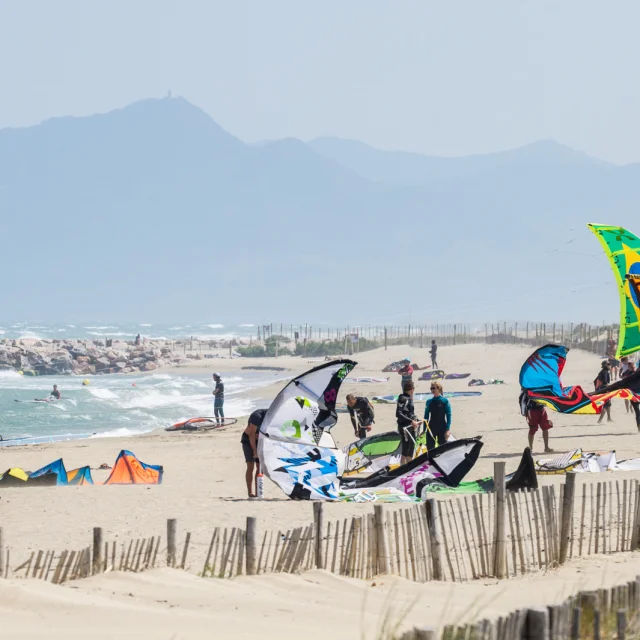 Plage ventée avec pratiquants installant leurs ailes de kitesurf près du rivage.
