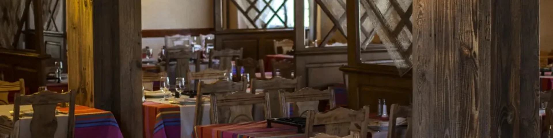 Salle de restaurant avec tables dressées et nappes colorées dans un décor en bois chaleureux.