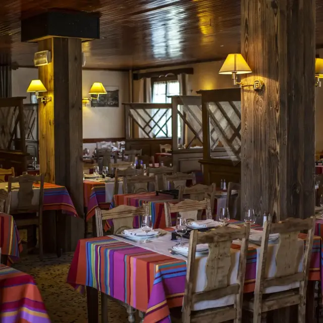 Salle de restaurant avec tables dressées et nappes colorées dans un décor en bois chaleureux.