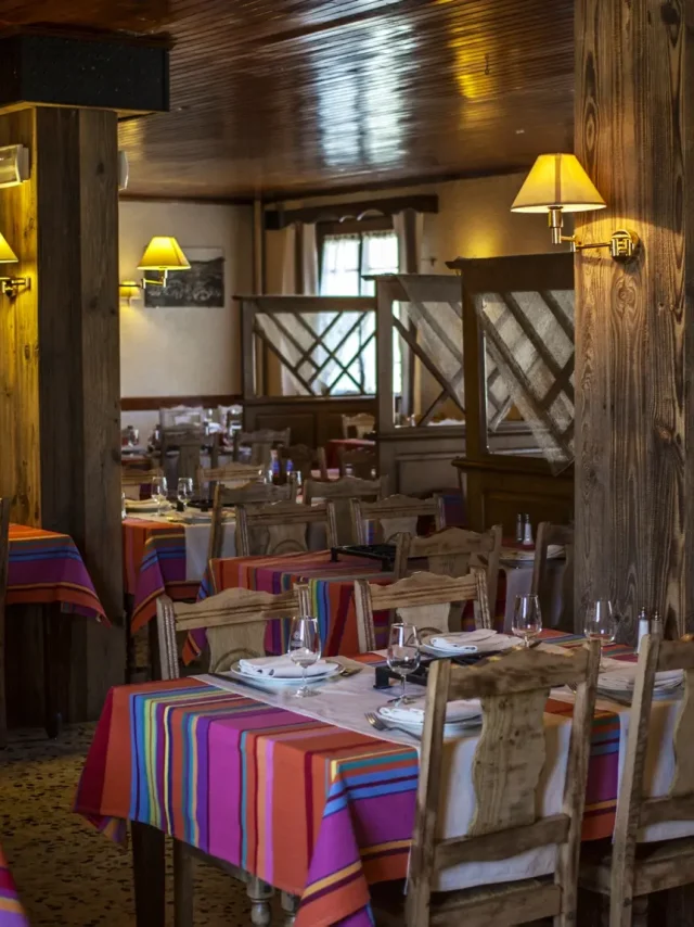 Salle de restaurant avec tables dressées et nappes colorées dans un décor en bois chaleureux.