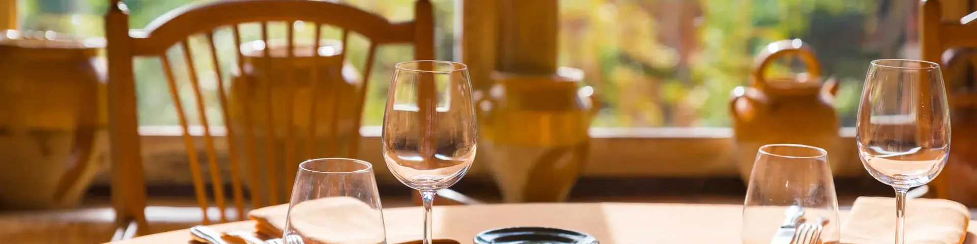 Table dressée avec verres et couverts devant une fenêtre donnant sur un jardin.