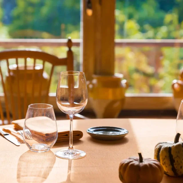 Table dressée avec verres et couverts devant une fenêtre donnant sur un jardin.