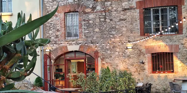 Façade en pierre du Relais de la Massane avec terrasse extérieure illuminée.