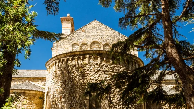 Abside en pierre d’une église romane entourée d’arbres.