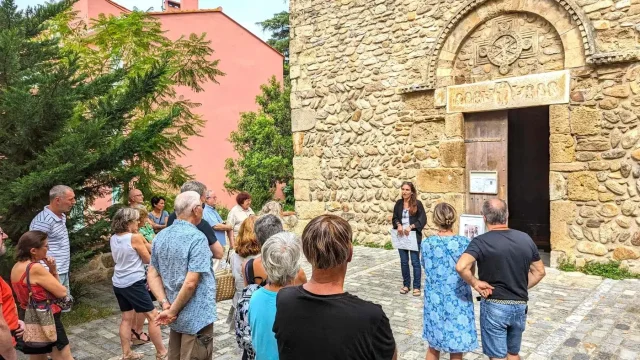 Groupe de visiteurs écoutant une guide devant l’entrée en pierre d’une église romane.