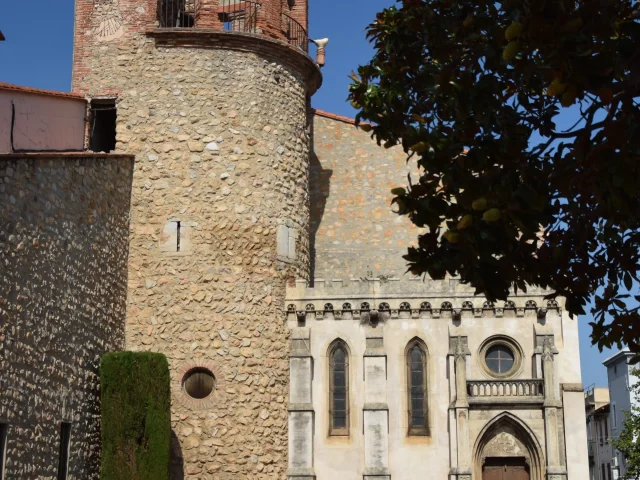 Place de la République à Thuir avec une tour ronde en pierre, une façade néogothique et un groupe de statues d’enfants.