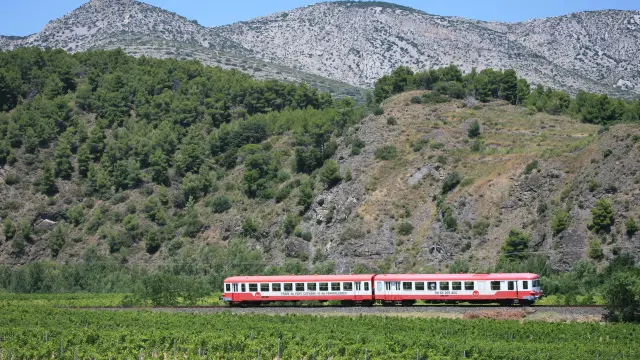 Train rouge traversant les vignes au pied des collines rocailleuses.