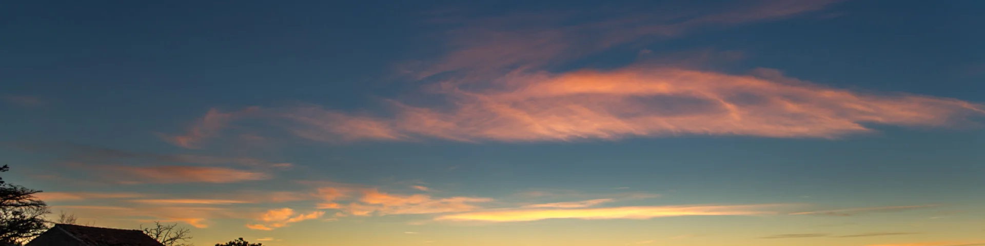 Paysage côtier au lever du soleil, avec vignes en terrasses au premier plan et mer éclairée par une lueur orange à l’horizon.
