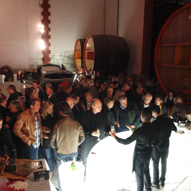 De nombreux visiteurs rassemblés pour une réception dans les Caves Byrrh à Thuir, entre grands foudres en bois et tables de dégustation.