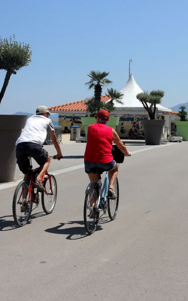 Deux cyclistes roulent sur une promenade aménagée en bord de mer.