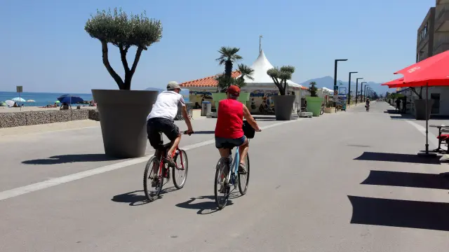 Deux cyclistes roulent sur une promenade aménagée en bord de mer.