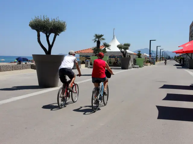 Deux cyclistes roulent sur une promenade aménagée en bord de mer.
