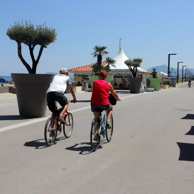Deux cyclistes roulent sur une promenade aménagée en bord de mer.