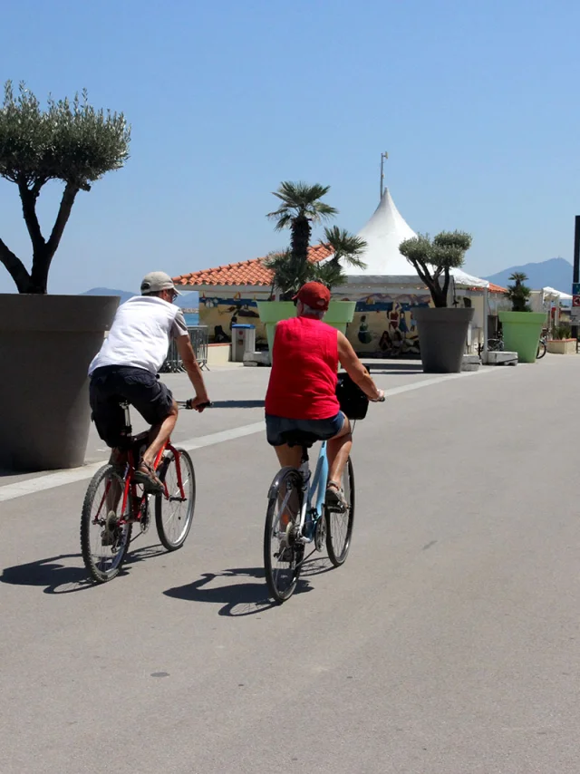 Deux cyclistes roulent sur une promenade aménagée en bord de mer.