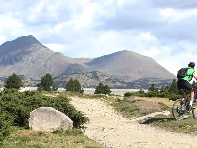 Cycliste avançant sur un sentier rocailleux en montagne, avec des pentes boisées et un large panorama en arrière-plan.