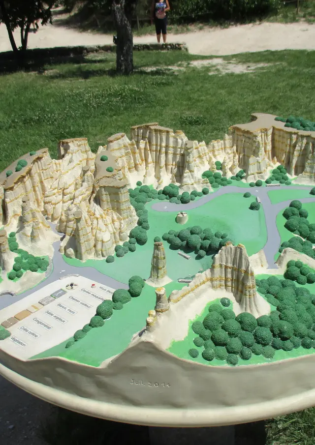 Maquette en relief représentant un site naturel avec falaises, sentiers et zones boisées.