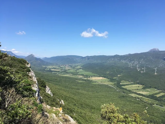 Panorama depuis un belvédère, montrant une vallée verdoyante entourée de montagnes et plusieurs éoliennes en crête.