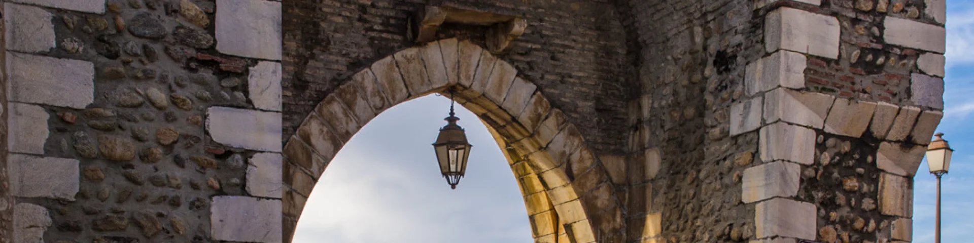 Porte médiévale en pierre formant une arche ouvrant sur les toits du village et les montagnes lointaines.
