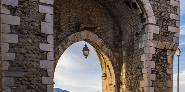 Porte médiévale en pierre formant une arche ouvrant sur les toits du village et les montagnes lointaines.