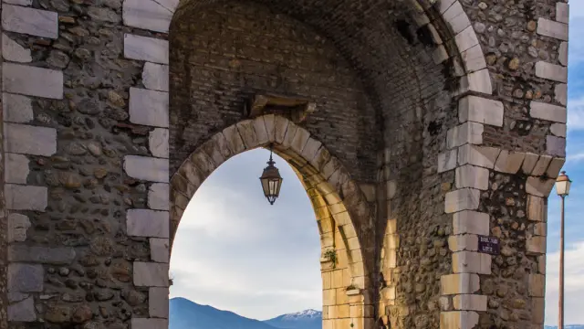 Porte médiévale en pierre formant une arche ouvrant sur les toits du village et les montagnes lointaines.