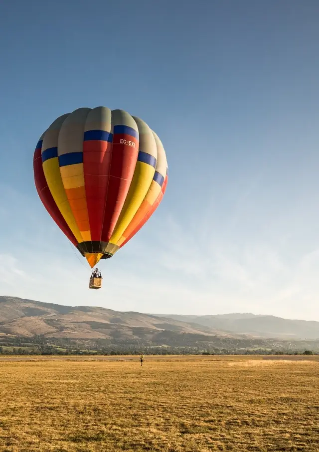 Montgolfière colorée en vol au-dessus de la plaine de Cerdagne, devant les montagnes.