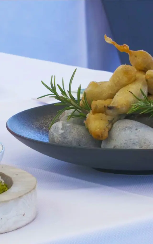 Assiette gastronomique avec beignets dorés dressés sur des galets, décorés de brins de romarin.