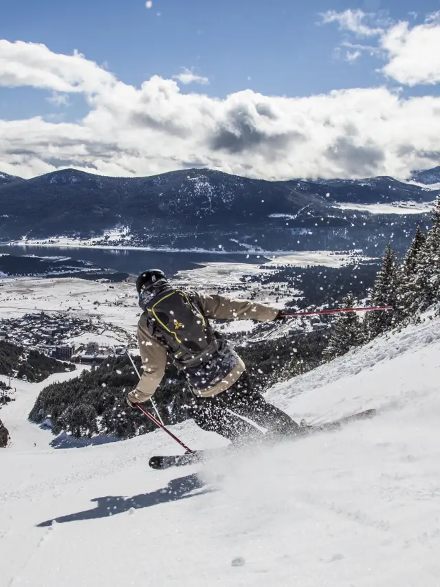 Skieur en descente sur une grande piste au-dessus du village enneigé des Angles et du lac de Matemale.