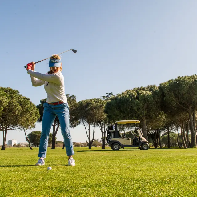 Golfeuse en plein swing sur le green du golf de Saint-Cyprien, sous un ciel bleu.