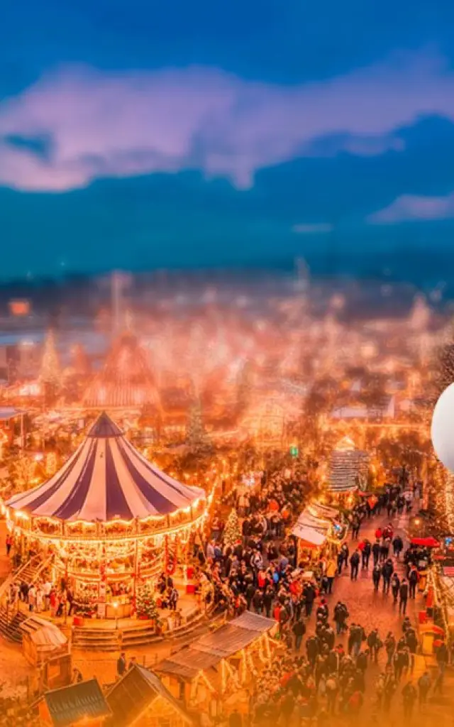 Illustration du Père Noël souriant devant une vue nocturne d’un village de Noël animé avec grande roue et manèges.