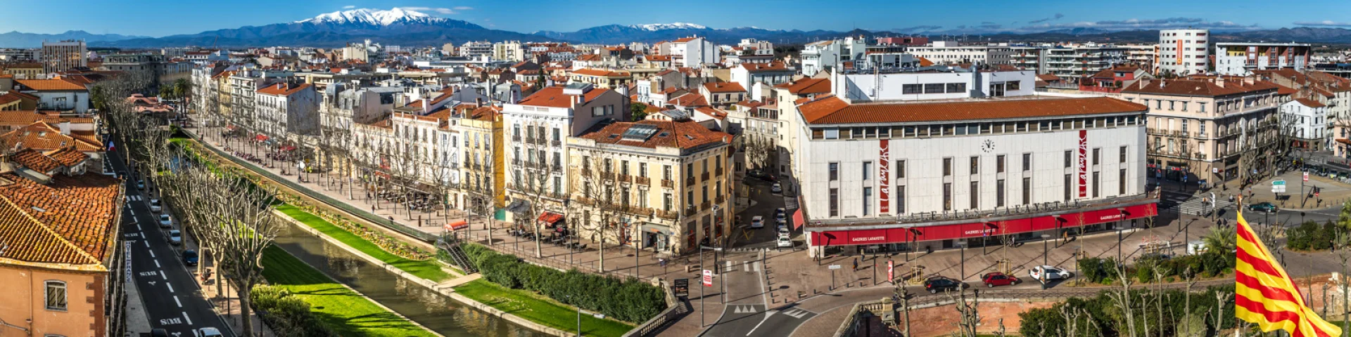 Vue panoramique de Perpignan avec le Canigou enneigé en arrière-plan.
