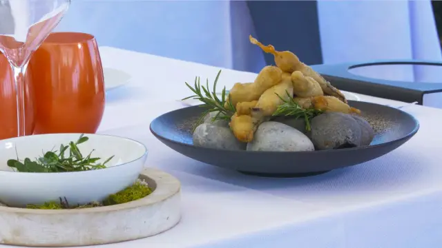 Assiette gastronomique avec beignets dorés dressés sur des galets, décorés de brins de romarin.