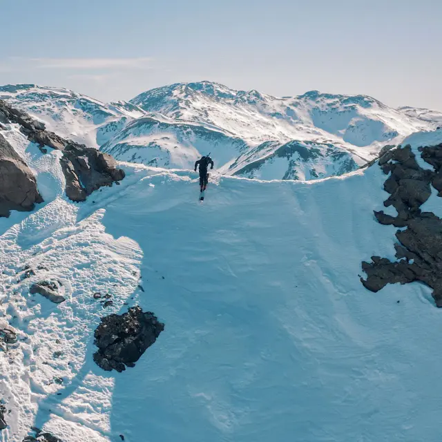 Sportif progressant sur une crête enneigée, entouré de hauts sommets de montagne.
