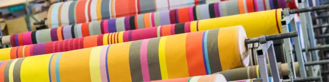 Rouleaux de tissus rayés très colorés alignés dans un atelier textile.
