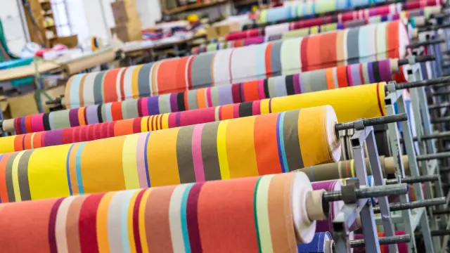 Rouleaux de tissus rayés très colorés alignés dans un atelier textile.