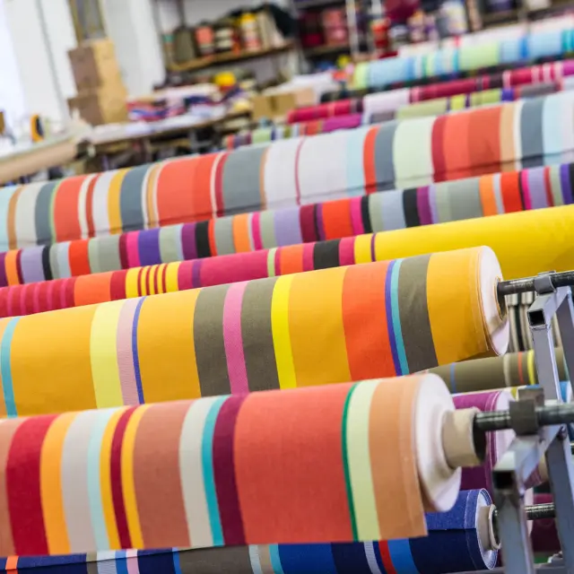 Rouleaux de tissus rayés très colorés alignés dans un atelier textile.