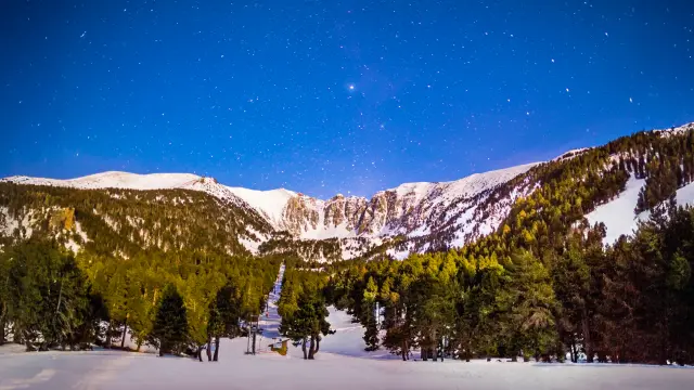 Ciel étoilé au-dessus du cirque enneigé du Cambre d’Aze et de la forêt de pins, vu depuis le plateau d’Eyne en hiver.