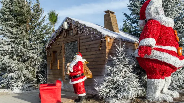 Chalet en bois décoré de neige artificielle avec statues du Père Noël et sapins givrés au marché de Noël du Barcarès.
