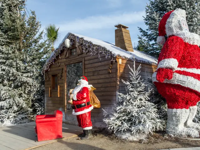 Chalet en bois décoré de neige artificielle avec statues du Père Noël et sapins givrés au marché de Noël du Barcarès.