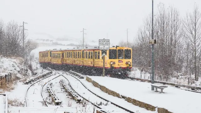 Le Train Jaune aux couleurs jaune et rouge de la SNCF entrant en gare de Bolquère sous une chute de neige dense, sur des voies et un quai entièrement enneigés.