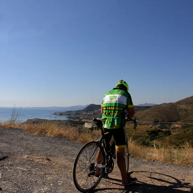 Cycliste à l’arrêt avec un vélo de route sur un point en hauteur, face à la mer et aux reliefs côtiers.