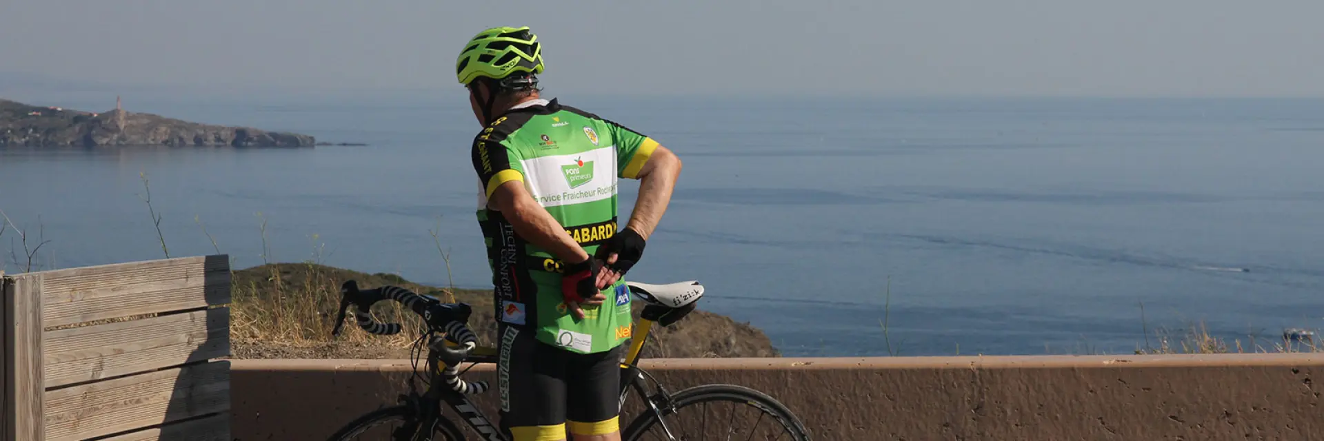 Cycliste à l’arrêt avec un vélo de route observant la mer Méditerranée depuis un point en hauteur.