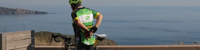 Cycliste à l’arrêt avec un vélo de route observant la mer Méditerranée depuis un point en hauteur.