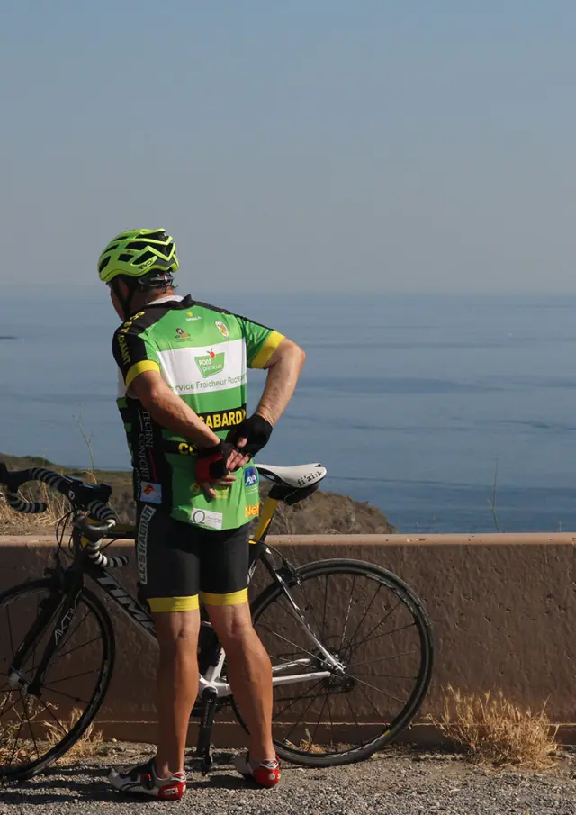 Cycliste à l’arrêt avec un vélo de route observant la mer Méditerranée depuis un point en hauteur.