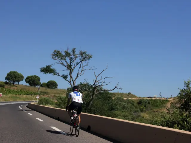 Cycliste roulant sur une route départementale bordée de végétation avec des collines en arrière-plan.